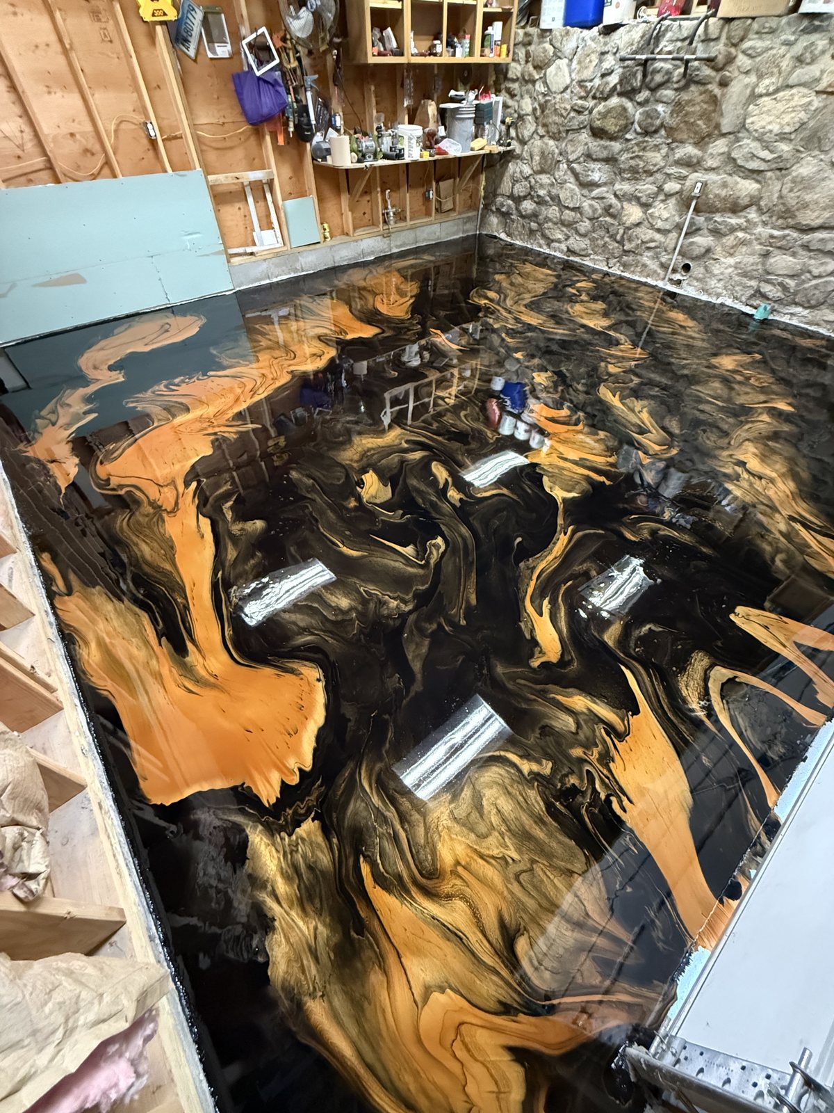 Gold and black metallic epoxy basement floor with a mirror gloss against a stone wall